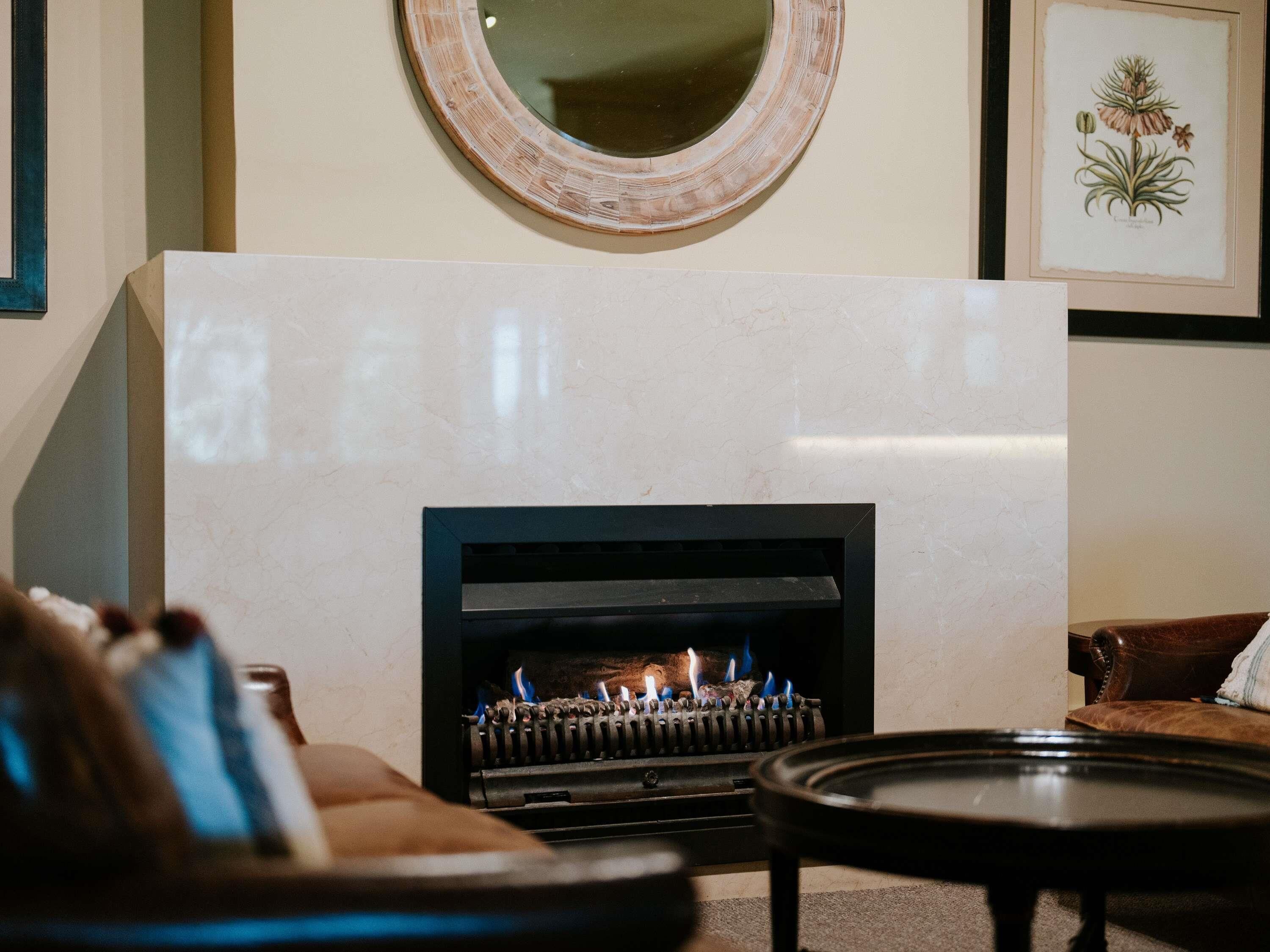 A living room with a fireplace, a round mirror, and a framed botanical illustration on the wall.