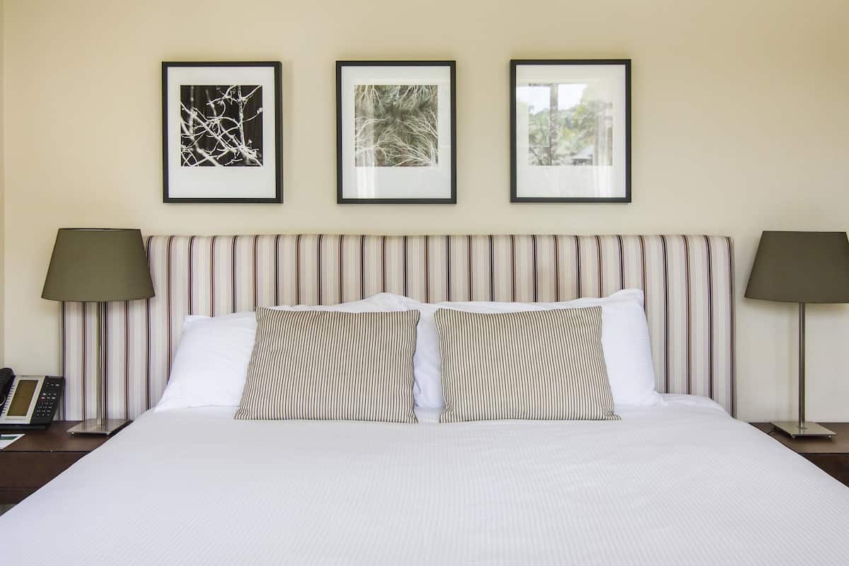 A hotel room with a bed, striped headboard, two bedside lamps, and three framed pictures on the wall.