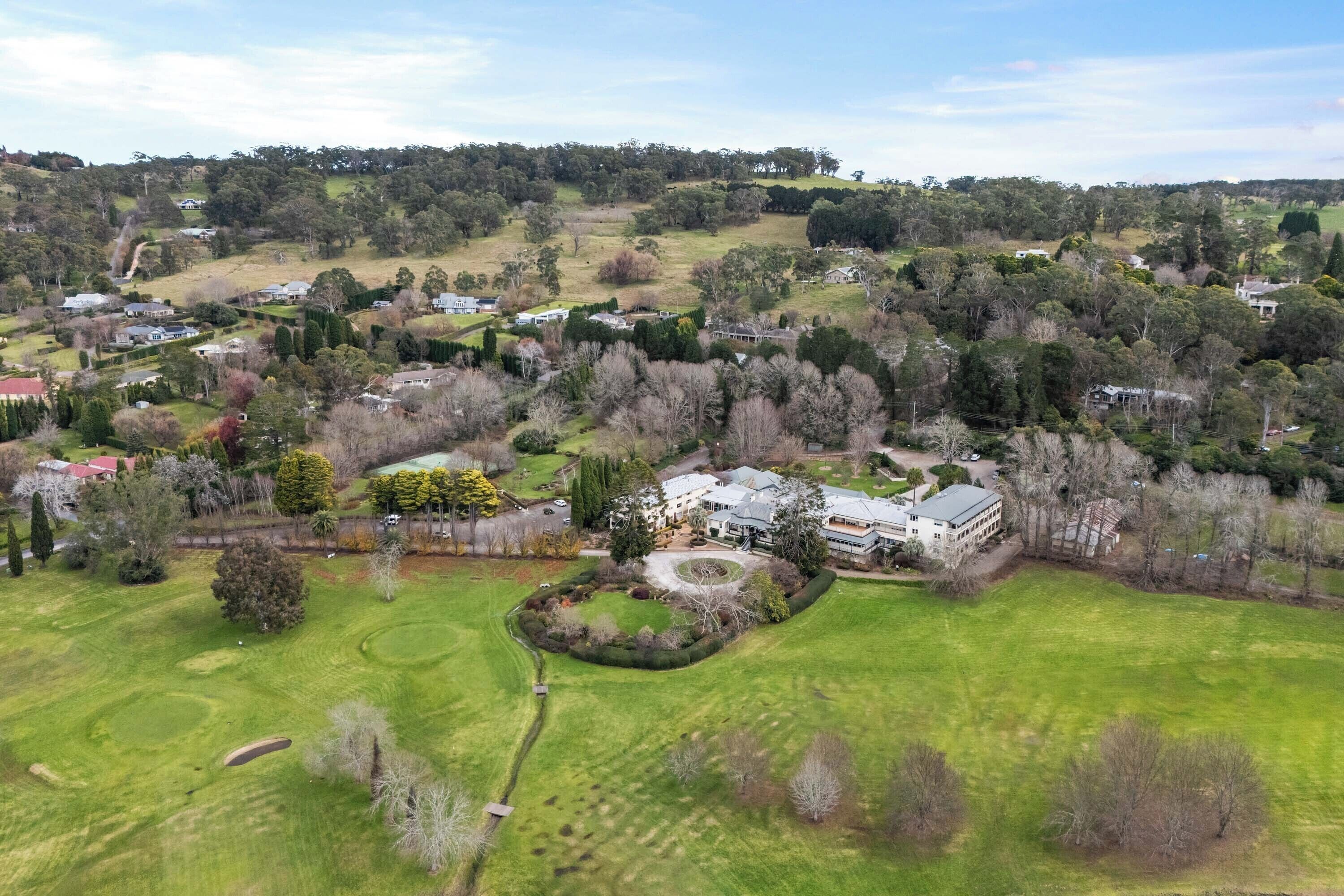 An aerial view of a residential area with houses, green lawns, and trees.
