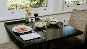 A dining table set with plates, glasses, and cutlery, a vase with a flower, and a view of greenery through a window. - Peppers Craigieburn (Bowral)