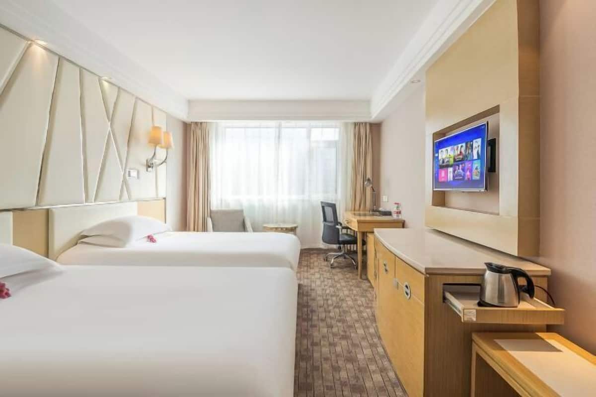 A hotel room with two beds, a desk, a television, and a coffee maker.