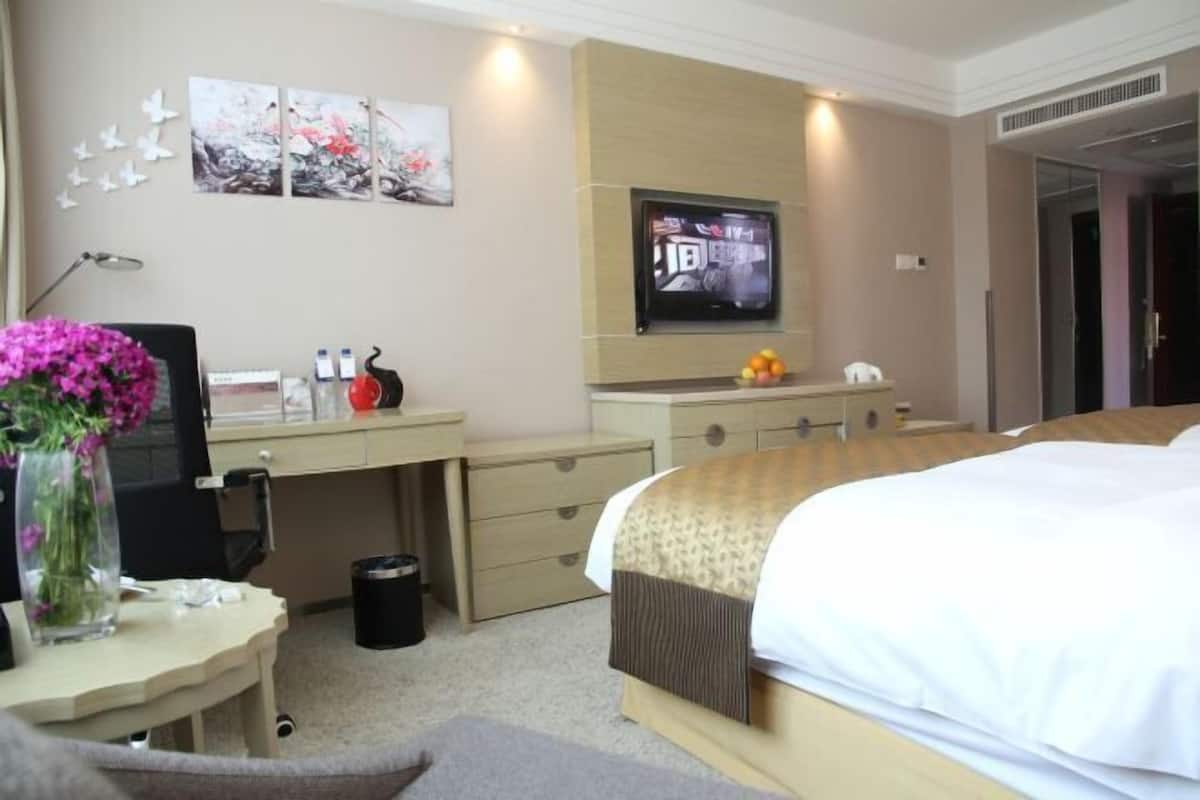 A hotel room with a bed, desk, TV, and artwork on the wall.