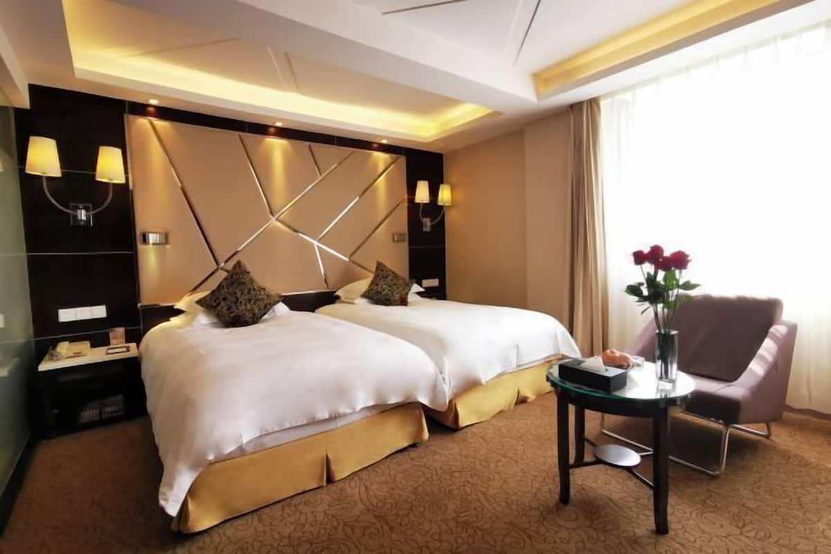 A hotel room with two beds, a small table, a chair, and a vase with flowers.