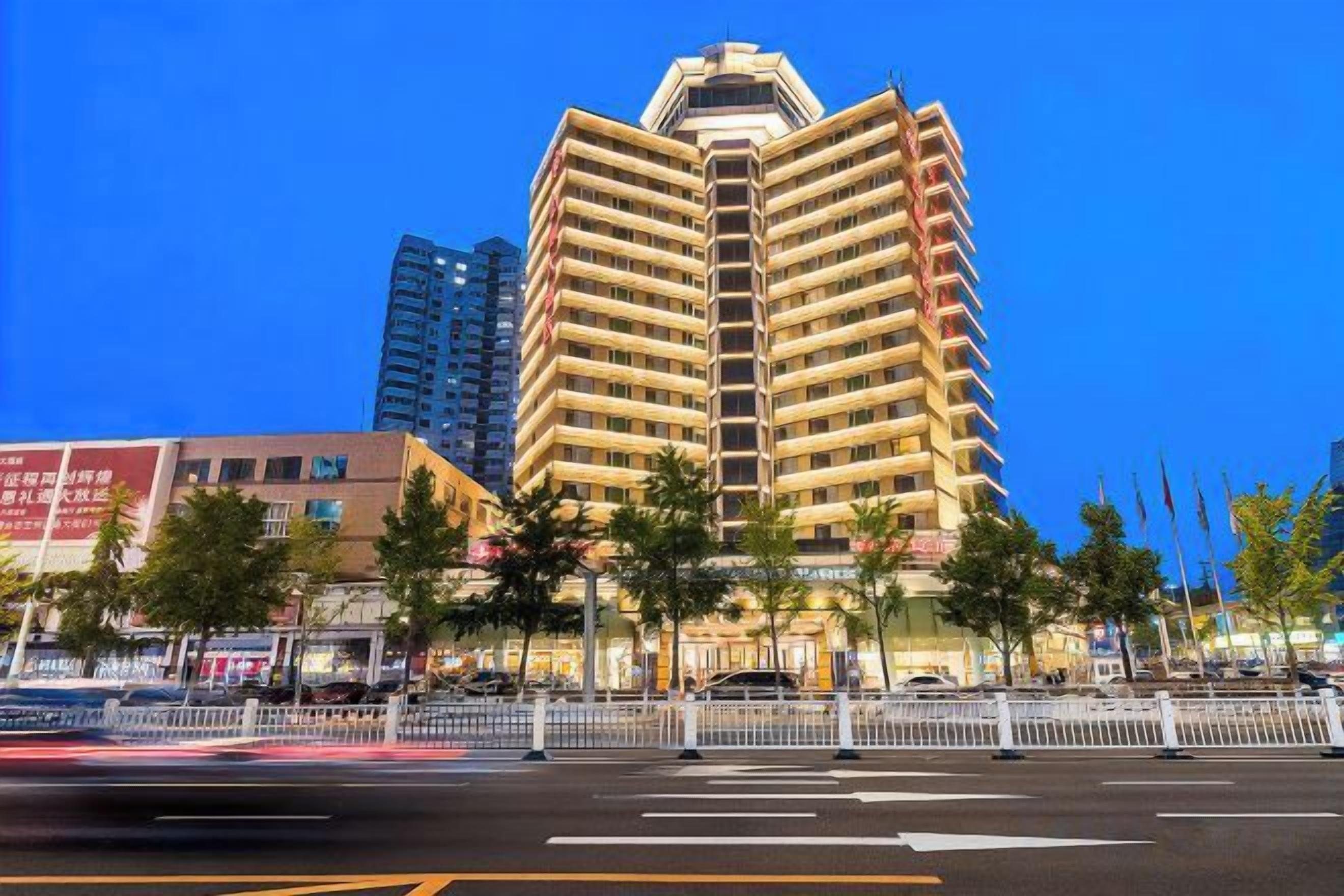 A multi-story hotel with a prominent corner location, surrounded by trees and a street view.