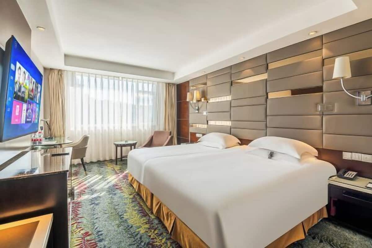 A hotel room with a large bed, a desk with a TV, a chair, and a window with curtains.