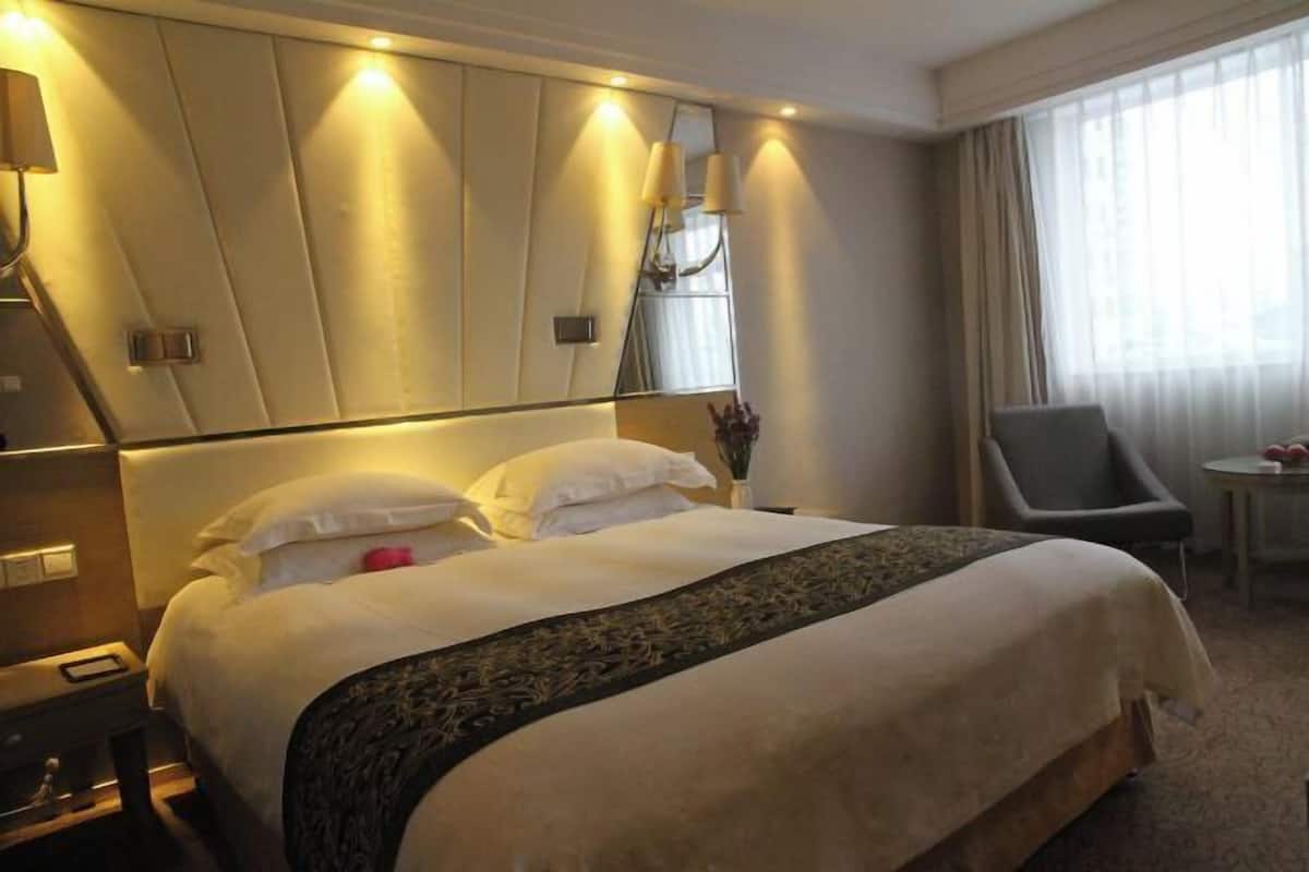 A hotel room with a large bed, a chair, a small table, and a mirror.