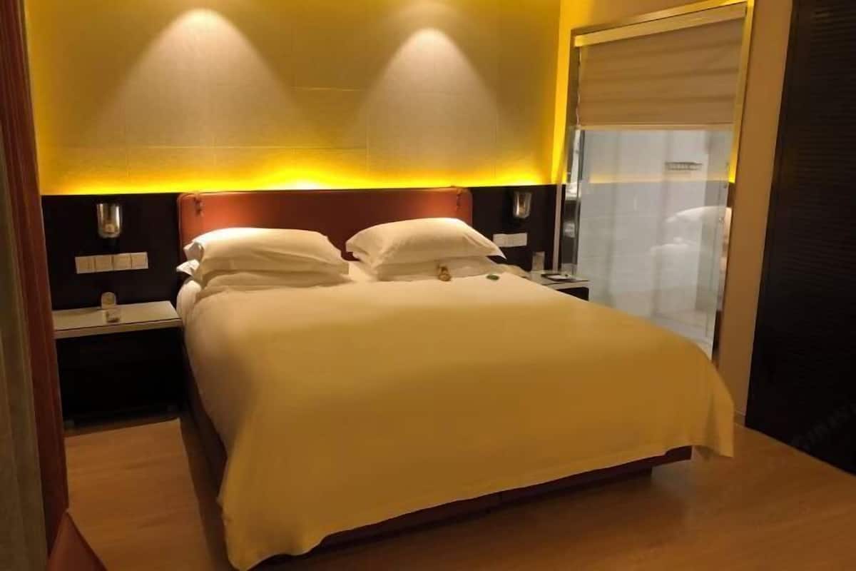 A hotel room with a bed, bedside tables, and a wall-mounted light fixture.