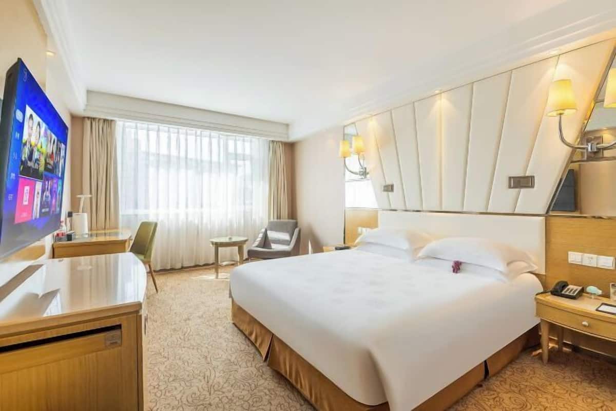 A hotel room with a large bed, a desk, a chair, and a television.
