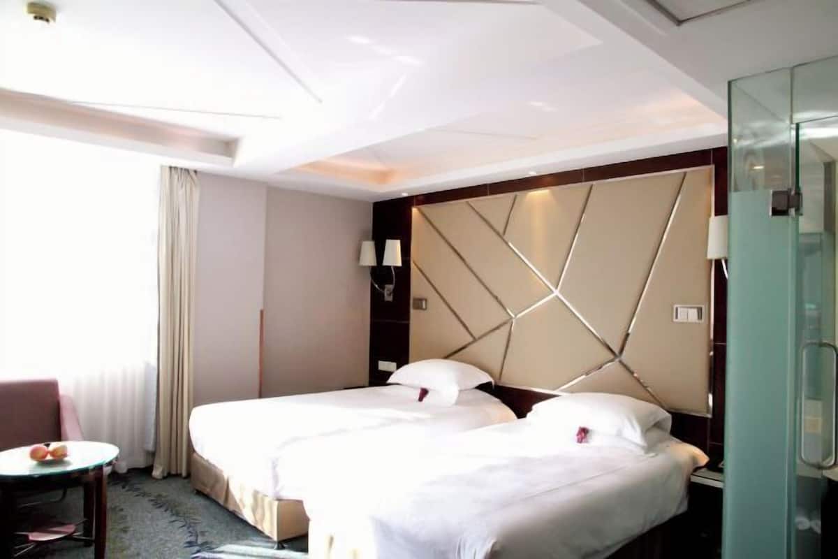 A hotel room with two beds, a glass shower enclosure, a small table with a chair, and a view of the outdoors.