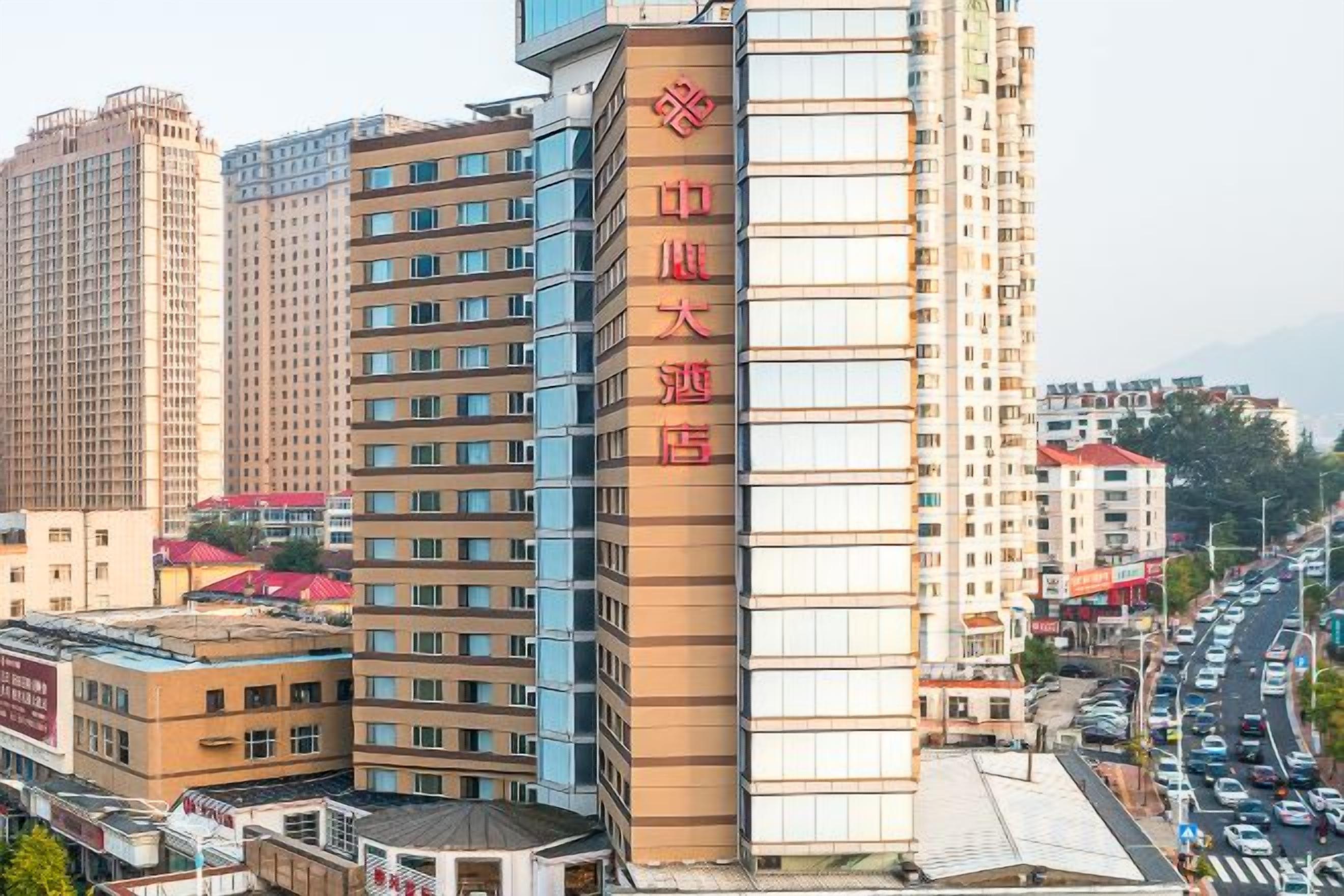 Un hotel de varios pisos con un llamativo letrero rojo en la fachada, varios pisos con balcones y una calle concurrida al fondo.