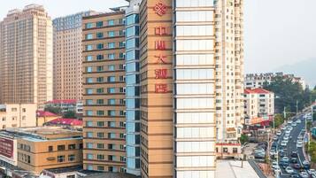 Un hotel de varios pisos con un llamativo letrero rojo en la fachada, varios pisos con balcones y una calle concurrida al fondo.