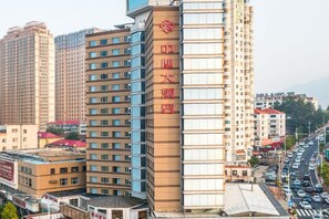 Ein mehrstöckiges Hotel mit auffälligem roten Schild an der Fassade, mehreren Etagen mit Balkonen und einer belebten Straße im Hintergrund.