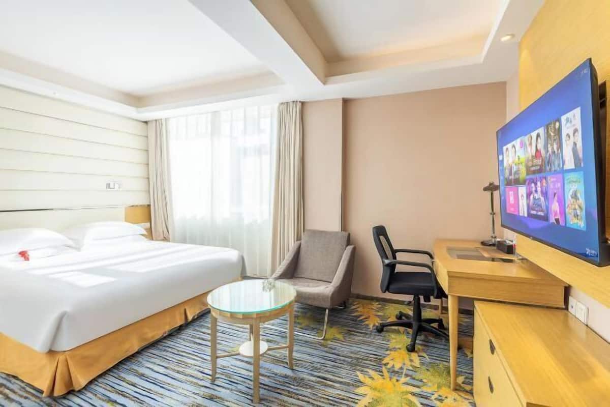 A hotel room with a bed, a desk, a chair, a television, and a small table.