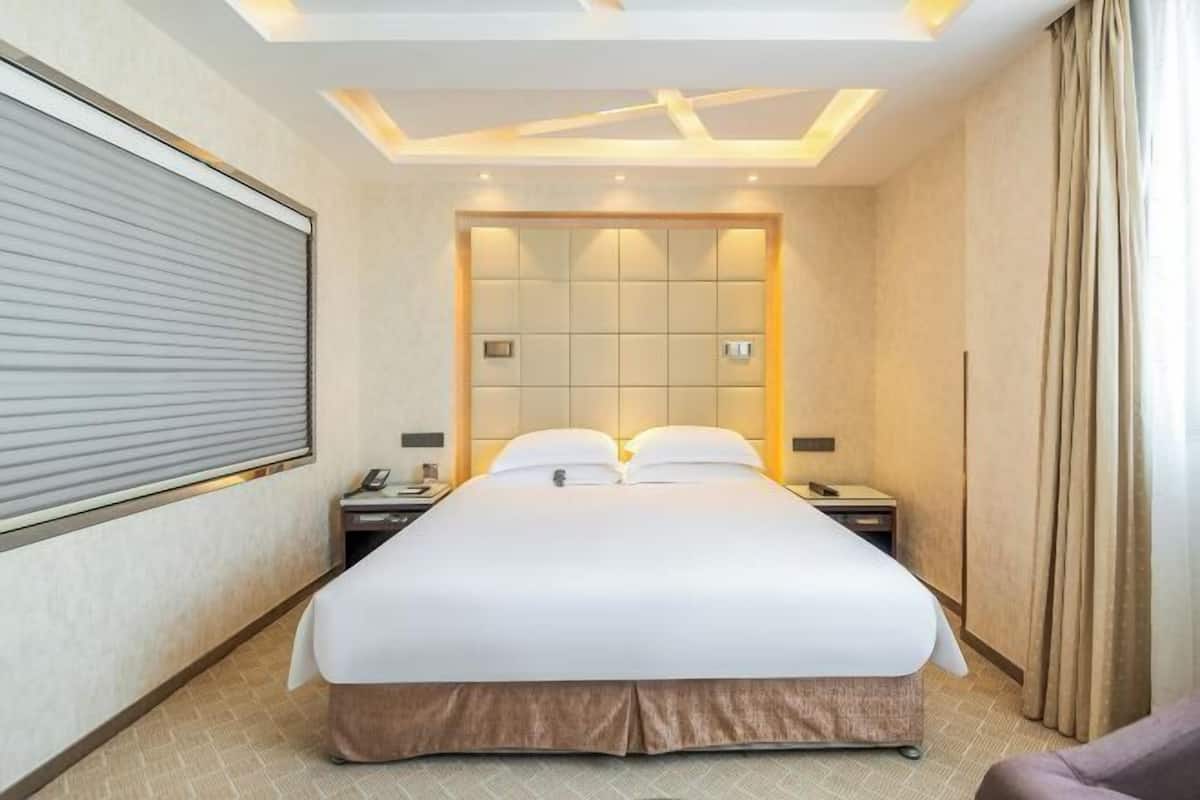 A hotel room with a bed, bedside tables, a headboard, and a window with curtains.