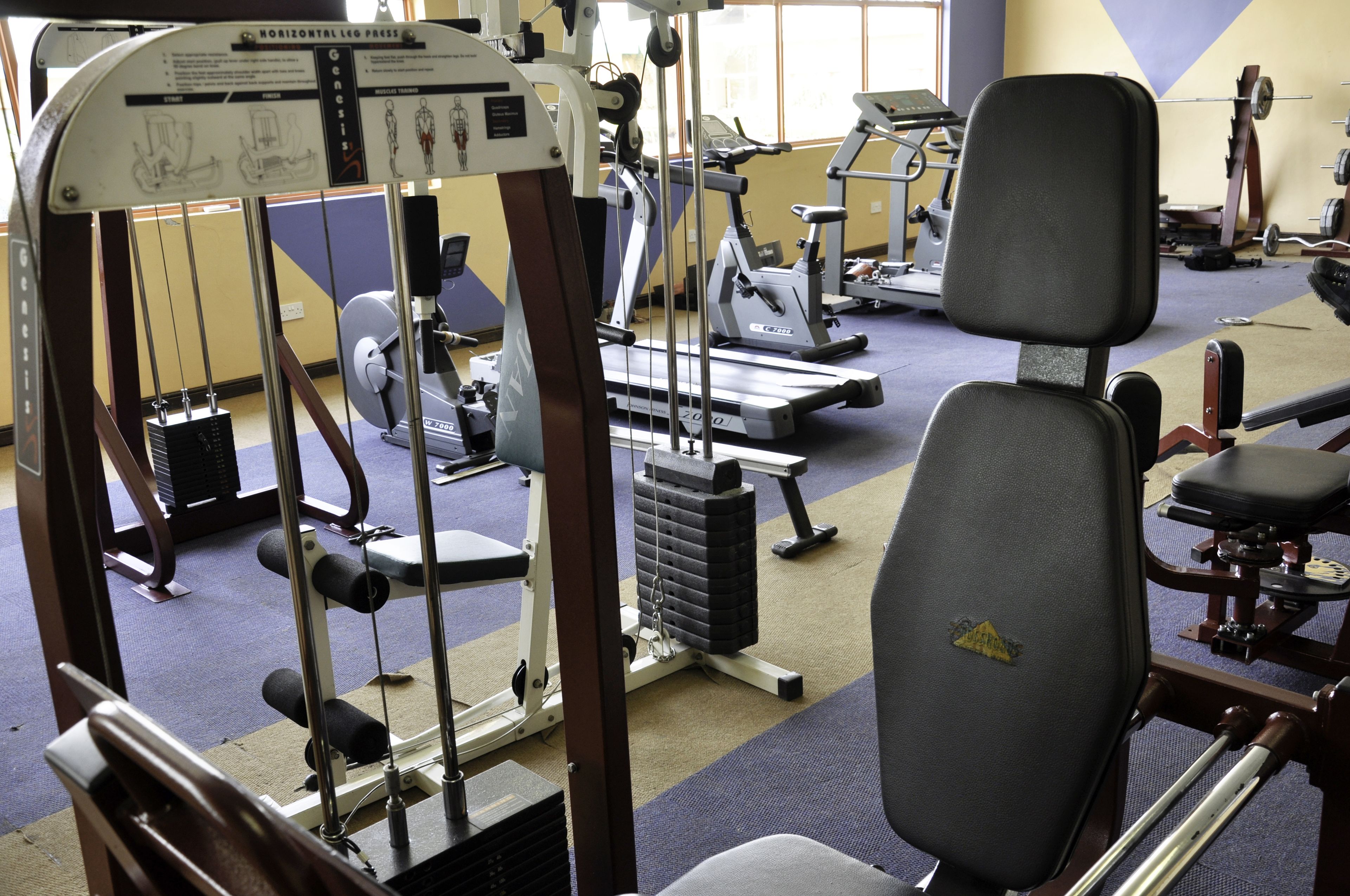 A gym with various exercise equipment including a leg press machine, treadmills, and weight benches.