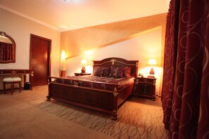 A hotel room with a large bed, two bedside tables with lamps, a wooden dresser, a chair, and a mirror on the wall. - Crossroads Hotel Lilongwe (Lilongwe)