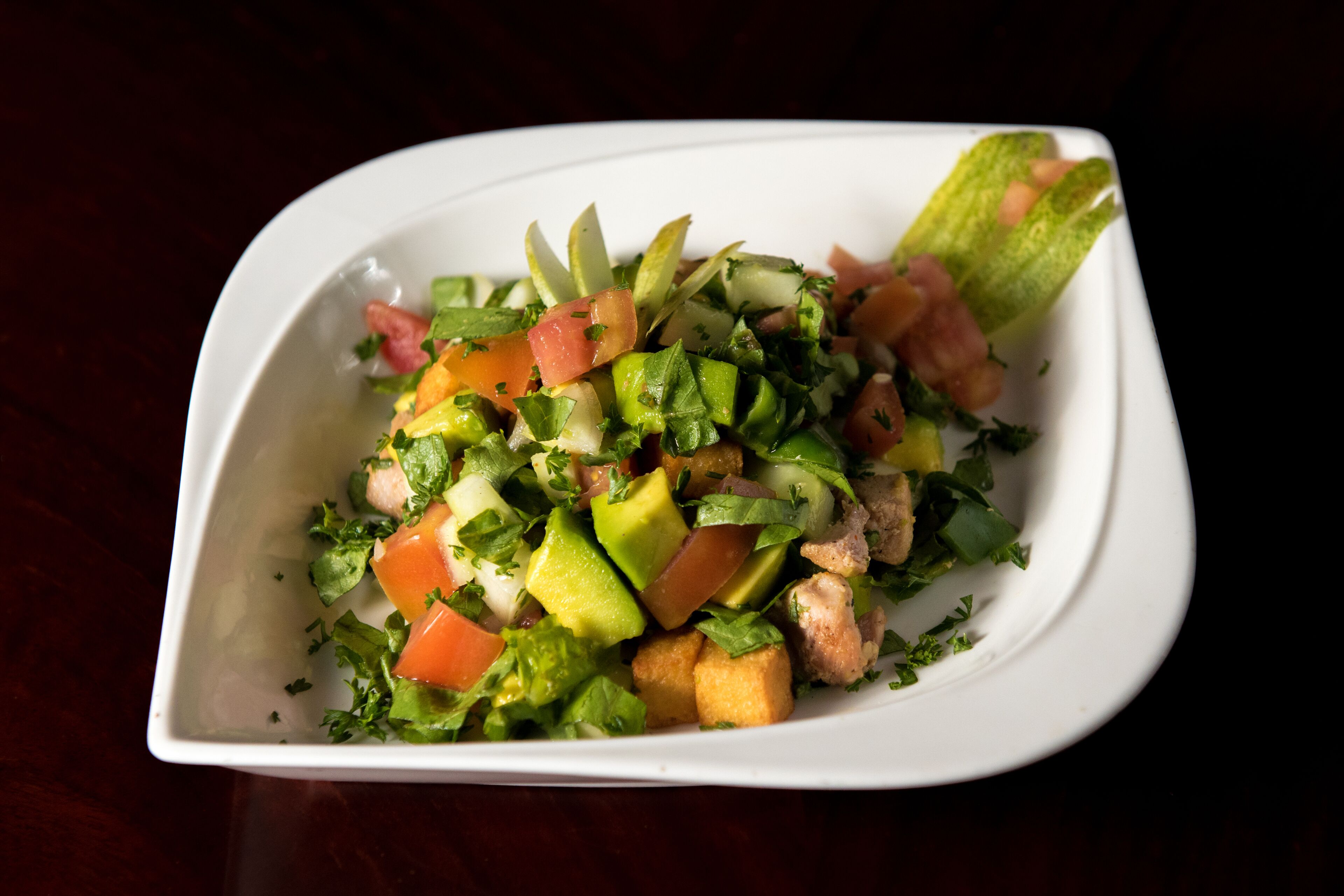 Un plat rectangulaire blanc contenant une salade composée de divers légumes et herbes aromatiques.