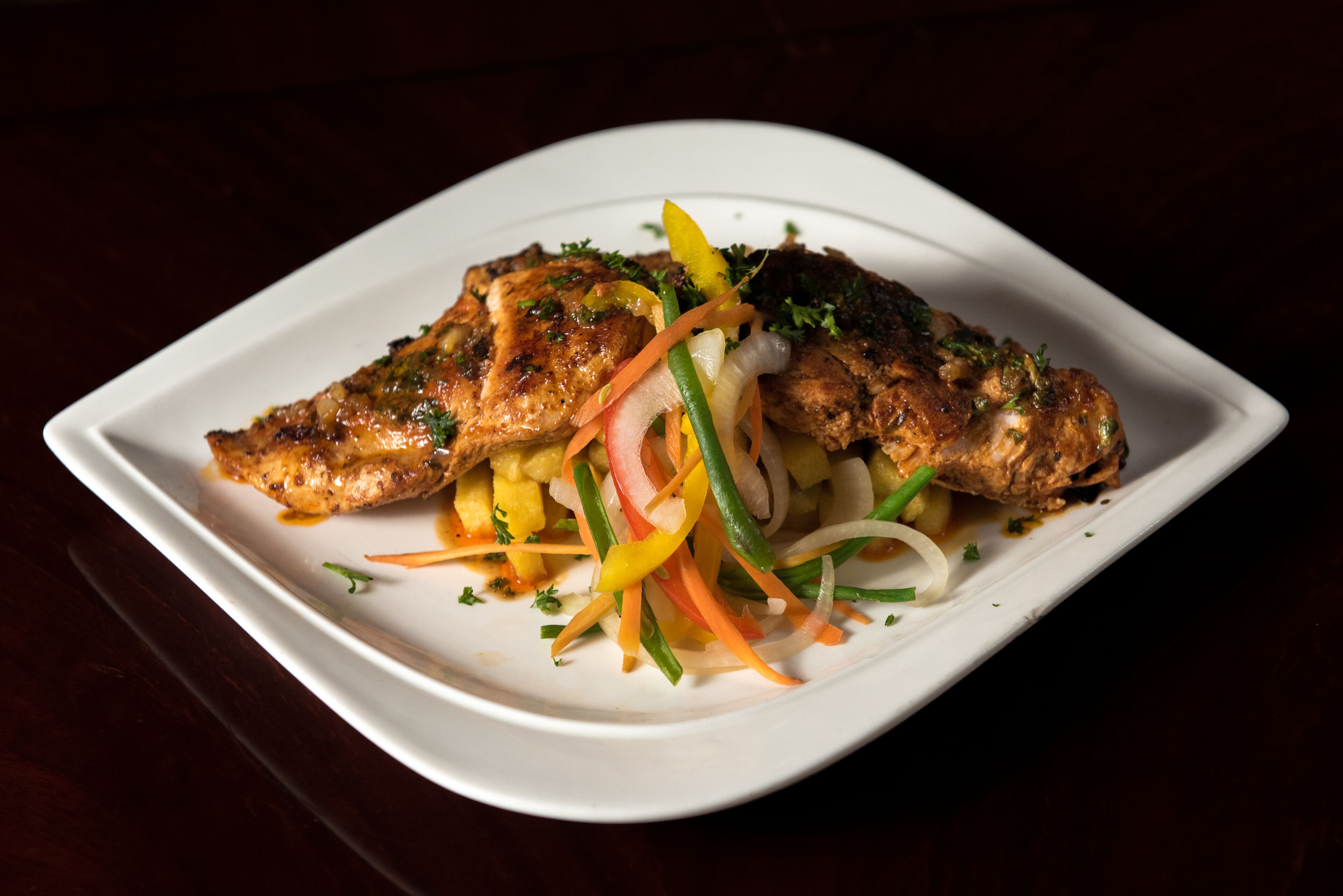 A white plate with grilled chicken and a colorful vegetable salad.