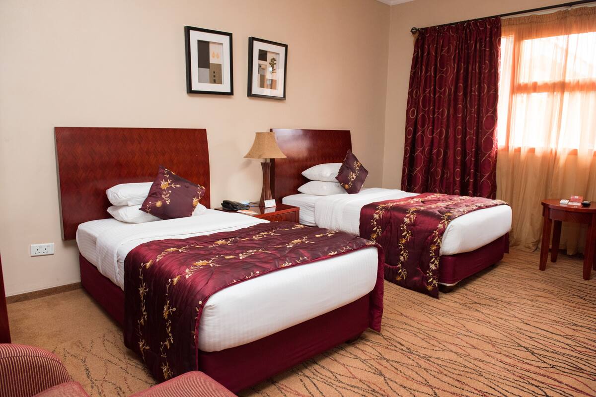 A hotel room with two beds, a nightstand, a lamp, and a small table.