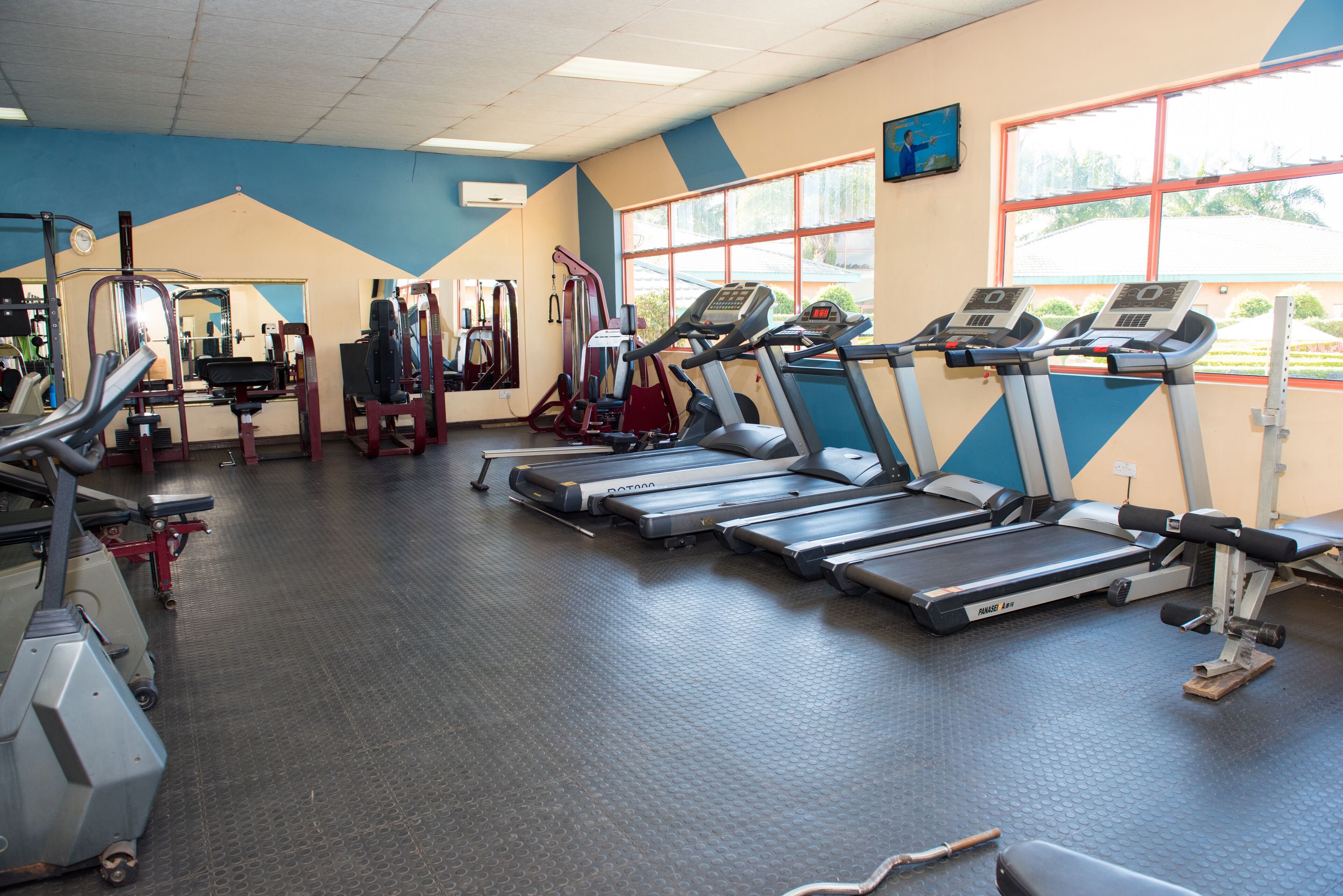 Un gimnasio con cintas de correr, máquinas de pesas y un espejo grande.