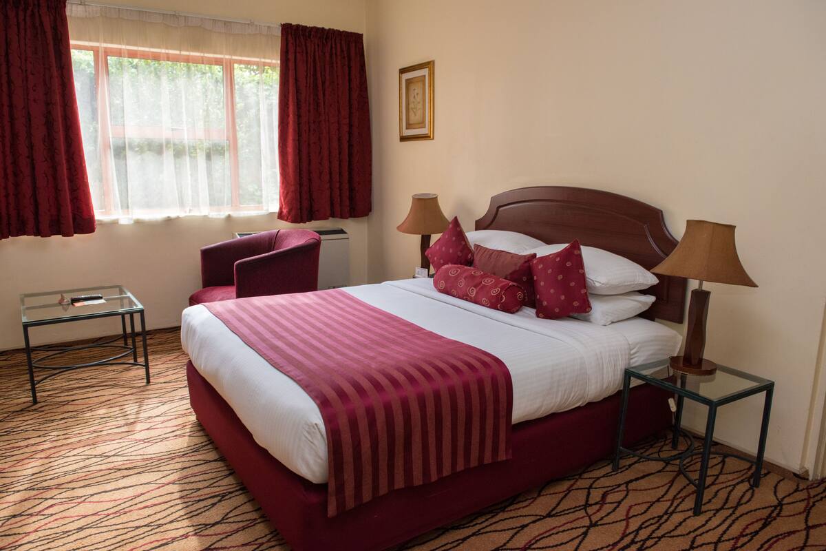 A hotel room with a large bed, two bedside tables, a chair, and a window with curtains.