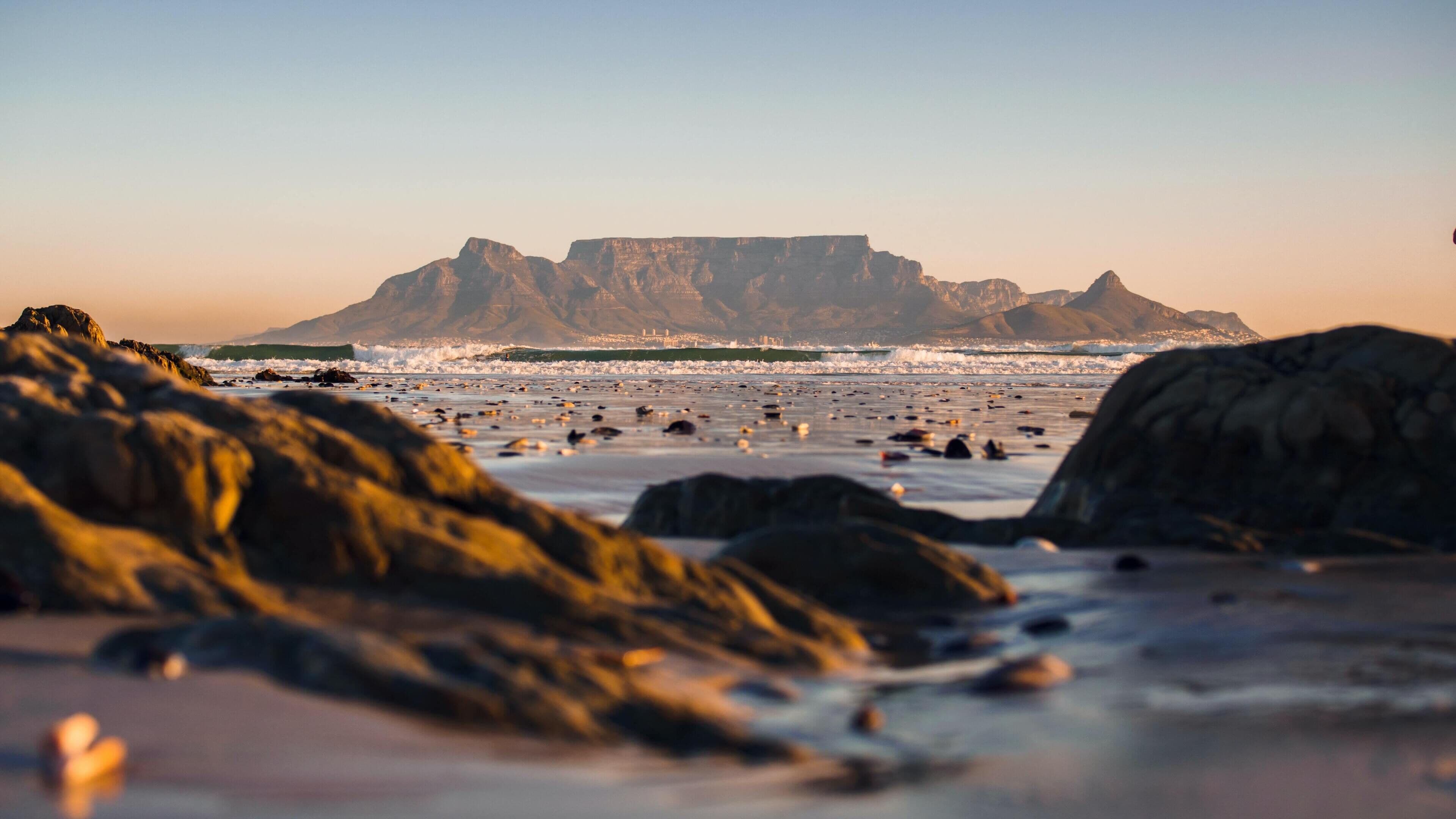 A beach with large rocks in the foreground and a mountain in the background.