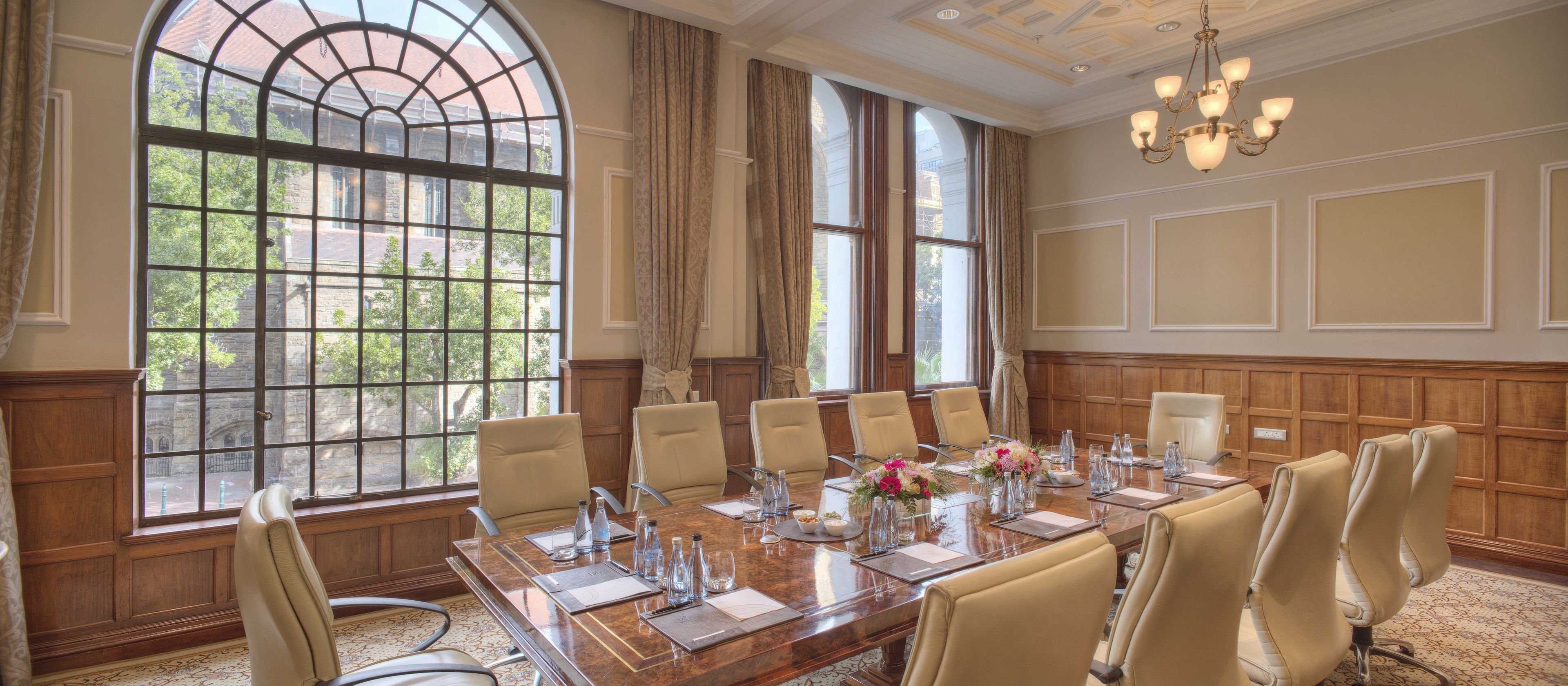 A conference room with a large table, multiple chairs, and a view of a building through large windows.