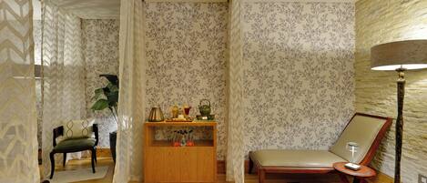 A room with a wooden bench, a small table with a lamp, and a decorative cabinet.
