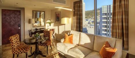 Ein Hotelzimmer mit Sofa, Sesseln, einem Esstisch und Blick auf die Stadt.