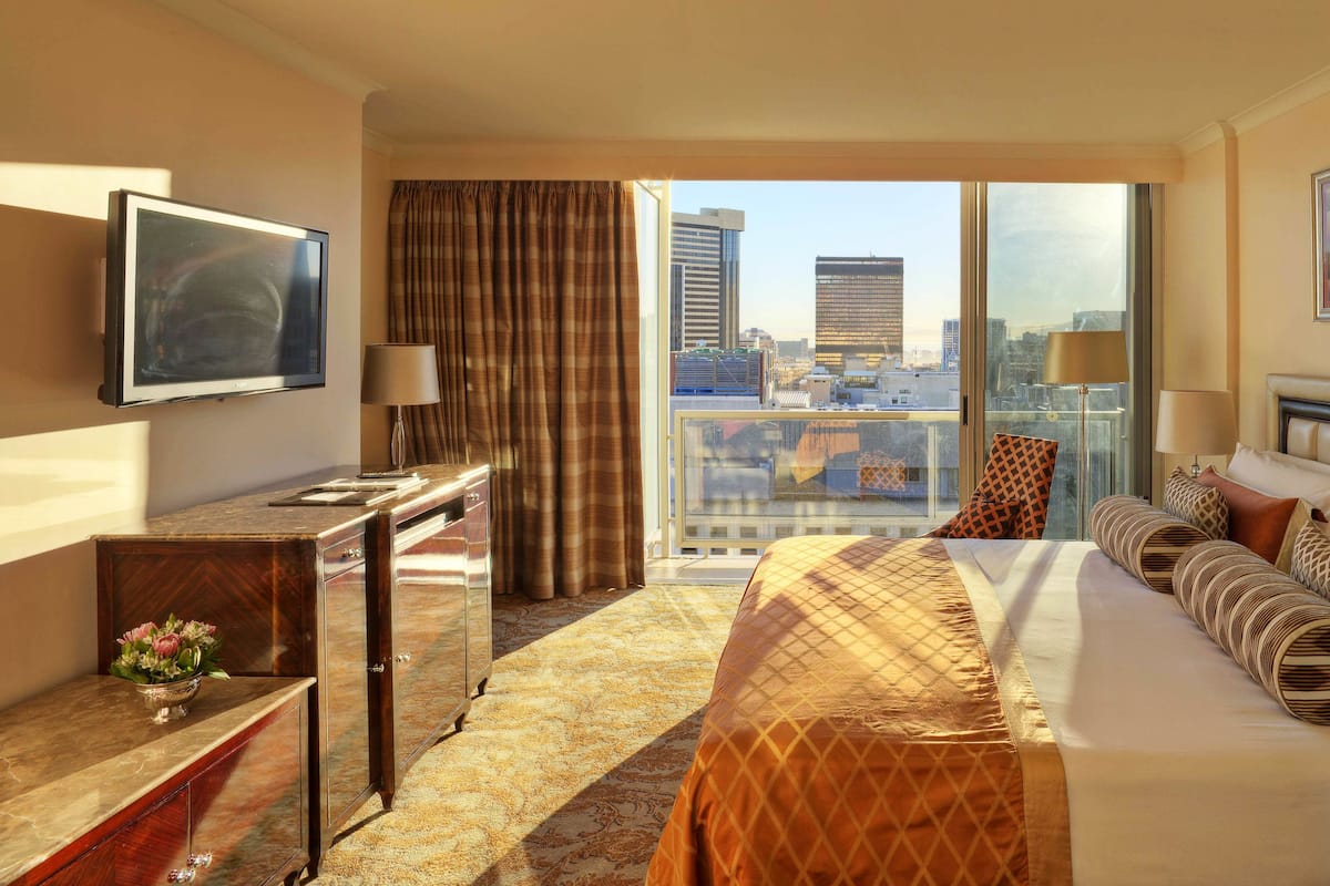 Une chambre d’hôtel avec un grand lit, un bureau, une télévision, une vue sur la ville et un balcon.