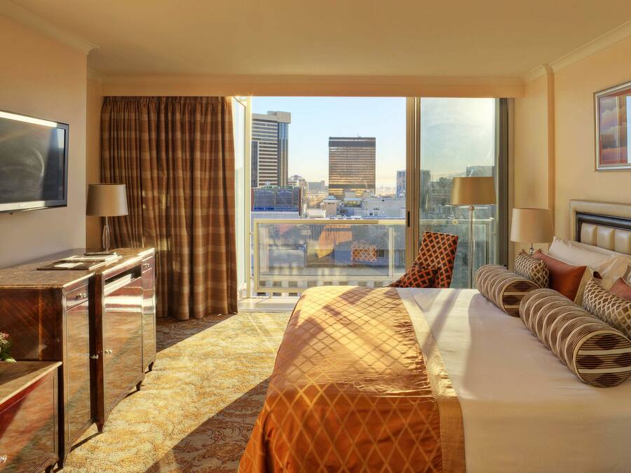 Habitación de hotel con una cama grande, escritorio, televisión, vistas de la ciudad y un balcón.