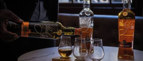 Une personne verse une boisson dans un verre posé sur une table, où se trouvent également plusieurs autres verres et bouteilles.