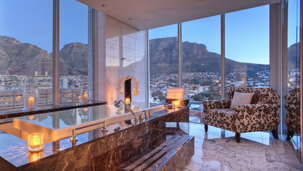 A modern bathroom with a large window, a marble sink, and a decorative chair. - Taj Cape Town (Cape Town)