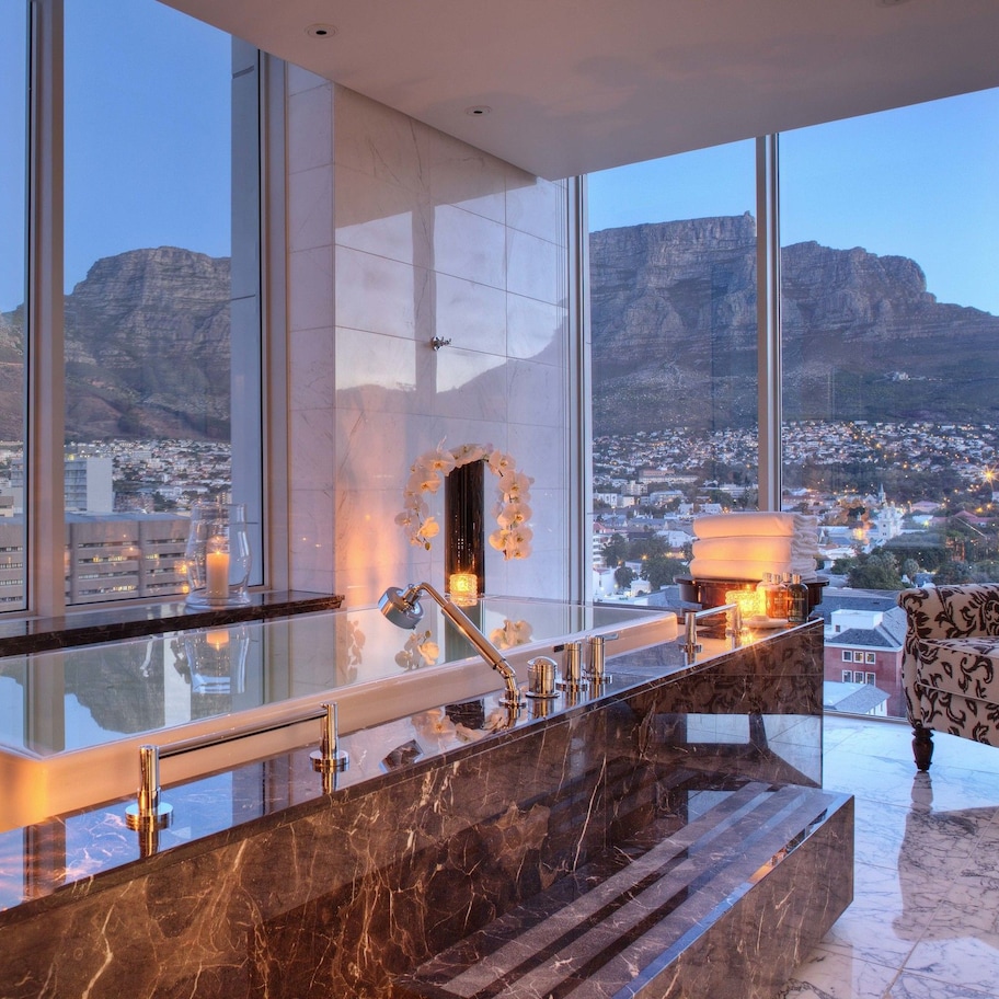 A modern bathroom with a large window, a marble sink, and a decorative chair.