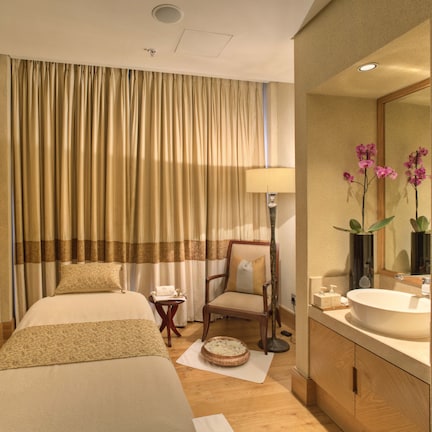 A hotel room with a bed, a chair, a bedside table with a lamp, a mirror, and a bathroom with a sink and mirror.