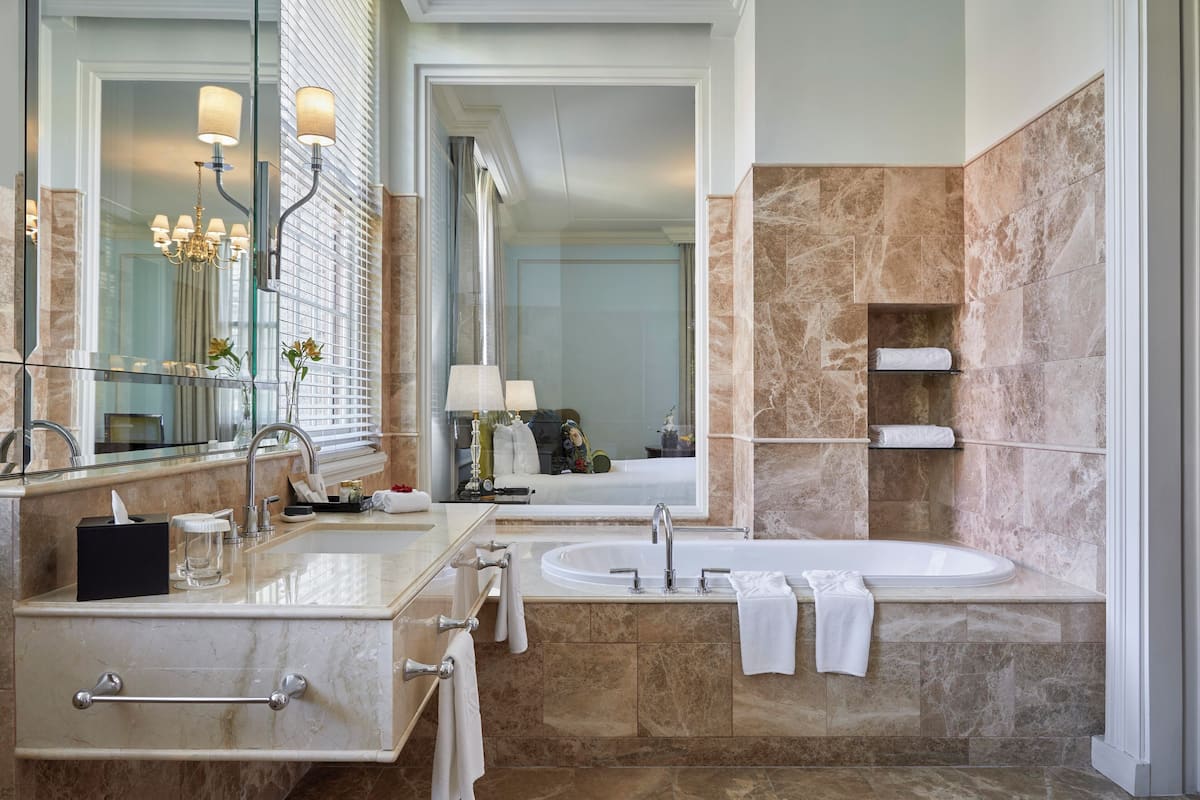 Une salle de bain moderne avec un grand miroir, un lavabo, une baignoire et des murs en marbre.