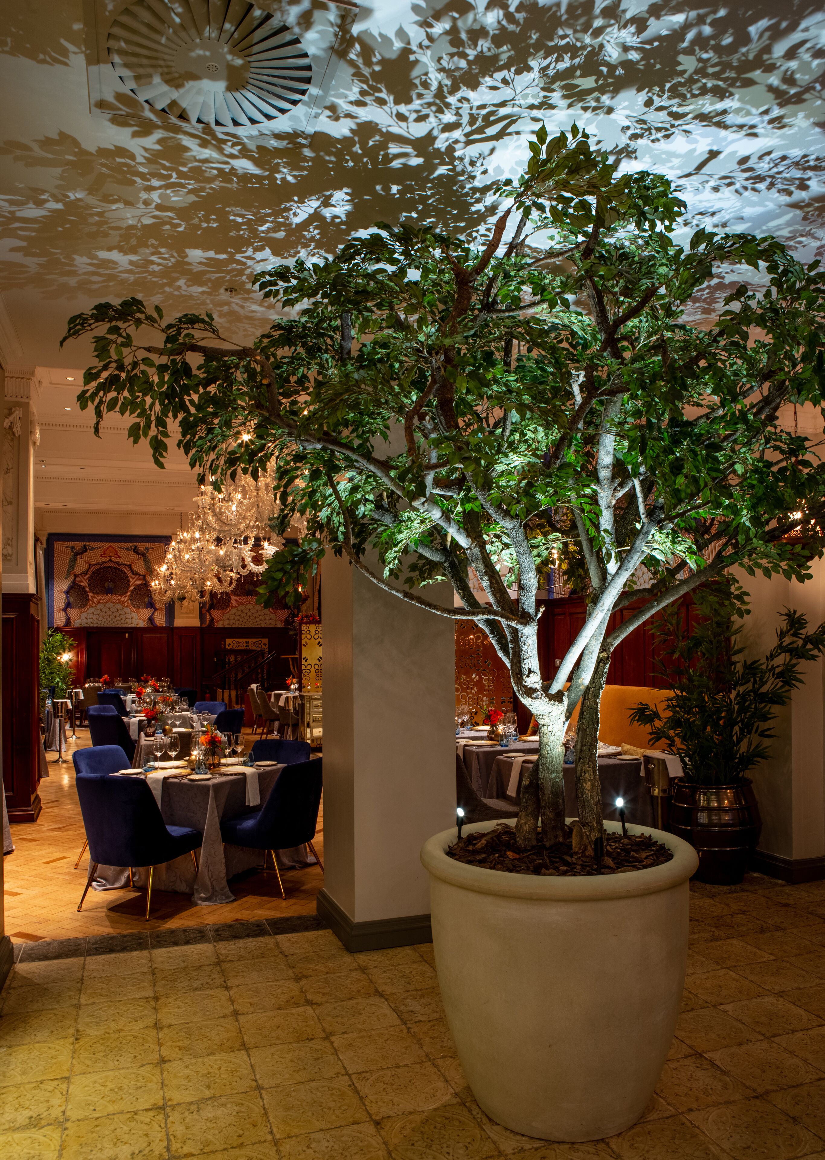 A large indoor tree in a well-lit dining area with tables set for a meal.