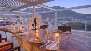 A dining table set with plates, glasses, and candles, overlooking a cityscape with mountains in the background. - Taj Cape Town (Cape Town)