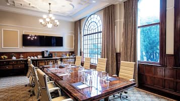 A conference room with a large table, chairs, a chandelier, a large window, and a flat-screen TV.