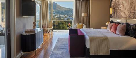 A modern hotel room with a large bed, a TV, a view of a mountain, and a balcony.