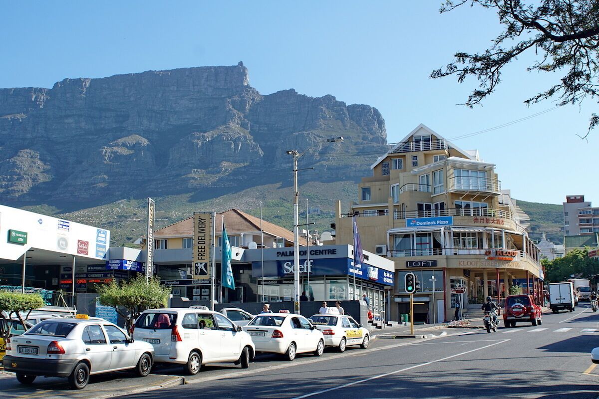 A street with parked cars, a building with a sign for Domino's Pizza, and a mountain in the background.