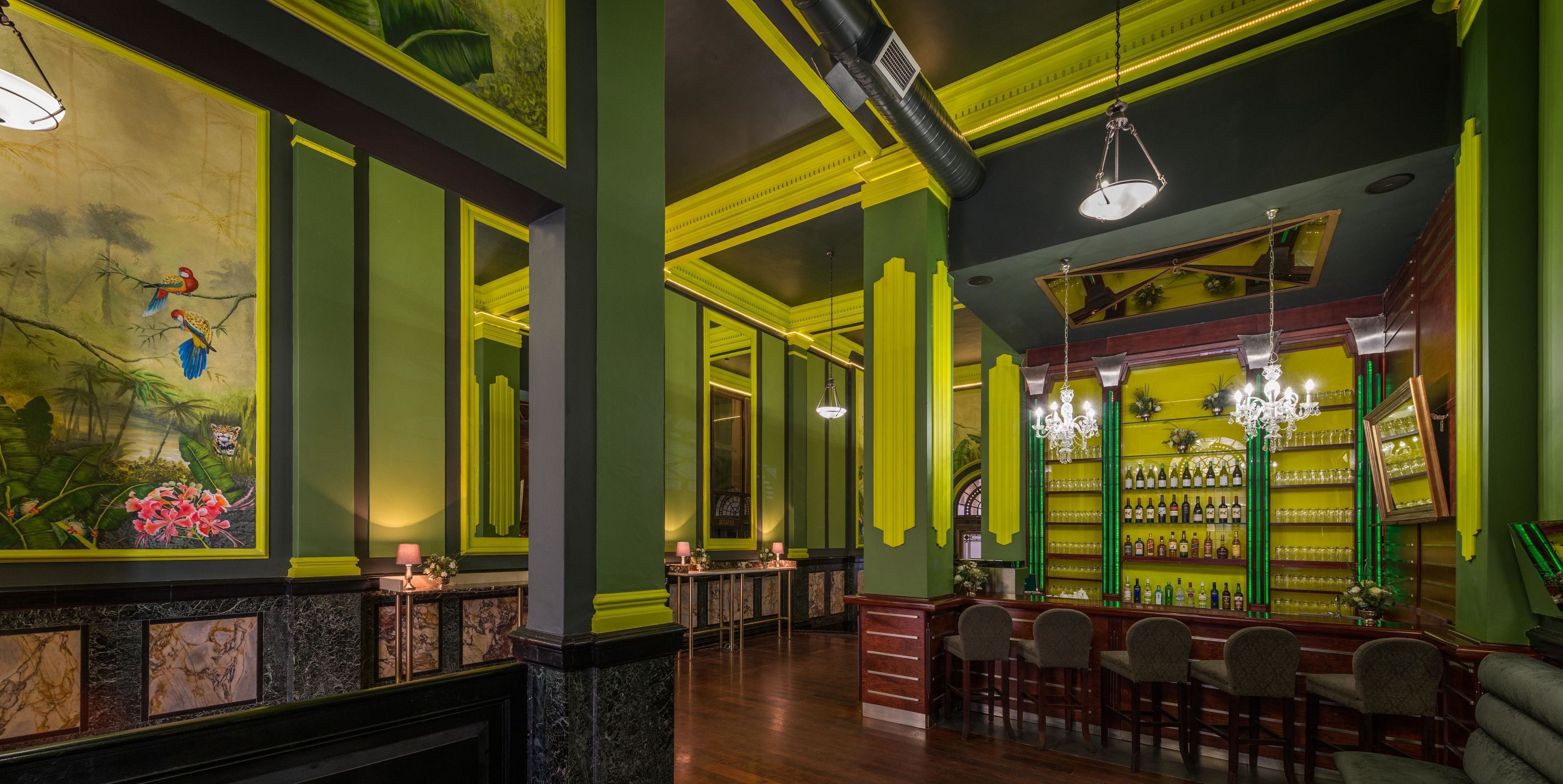 Uma área de bar com esquema de cores verde e amarelo, bancadas de mármore e diversos banquetas.