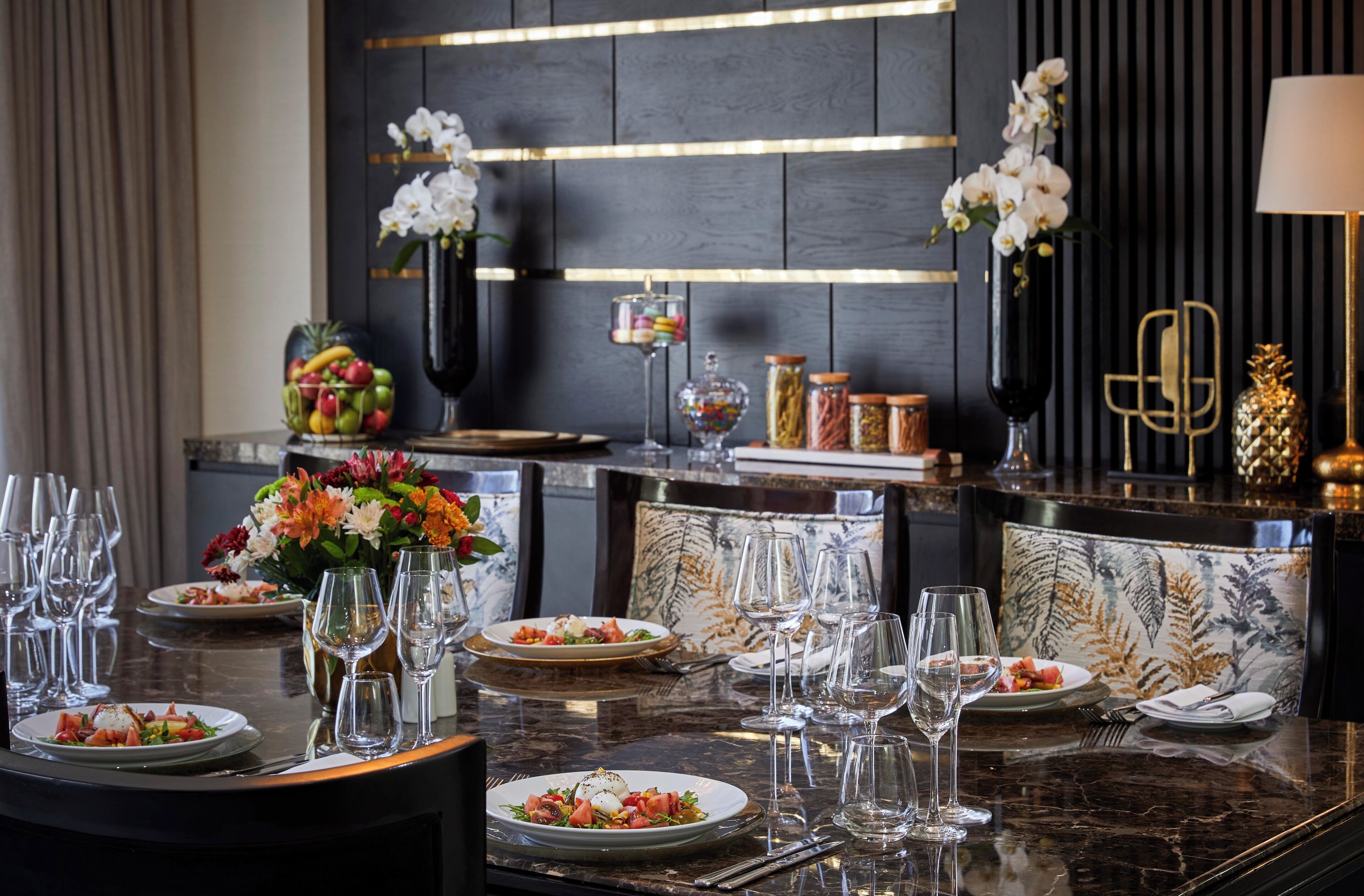 A dining area with a marble table set for a meal, featuring plates of food, wine glasses, and a vase with flowers.