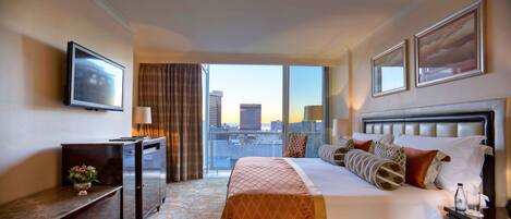 Una habitación de hotel con una cama grande, televisión, escritorio y vistas a la ciudad a través de la ventana.