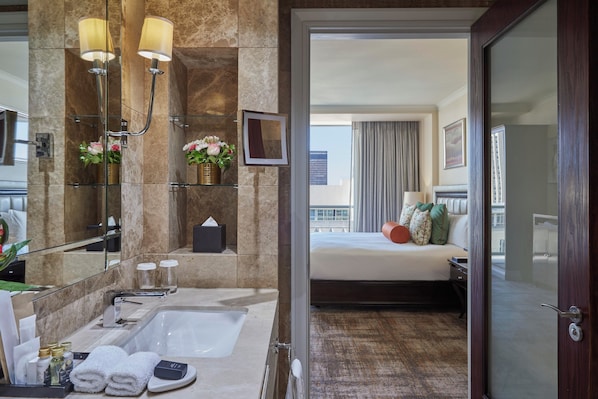 A modern hotel bathroom with a large sink, mirror, and two wall-mounted lamps. - Taj Cape Town (Cape Town)