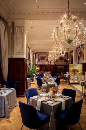 A formal dining room with chandeliers, tables set for dining, and a patterned wall.