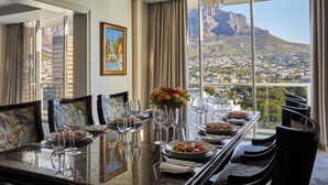A dining area with a table set for a meal, large windows with a mountain view, and a chandelier. - Taj Cape Town (Cape Town)