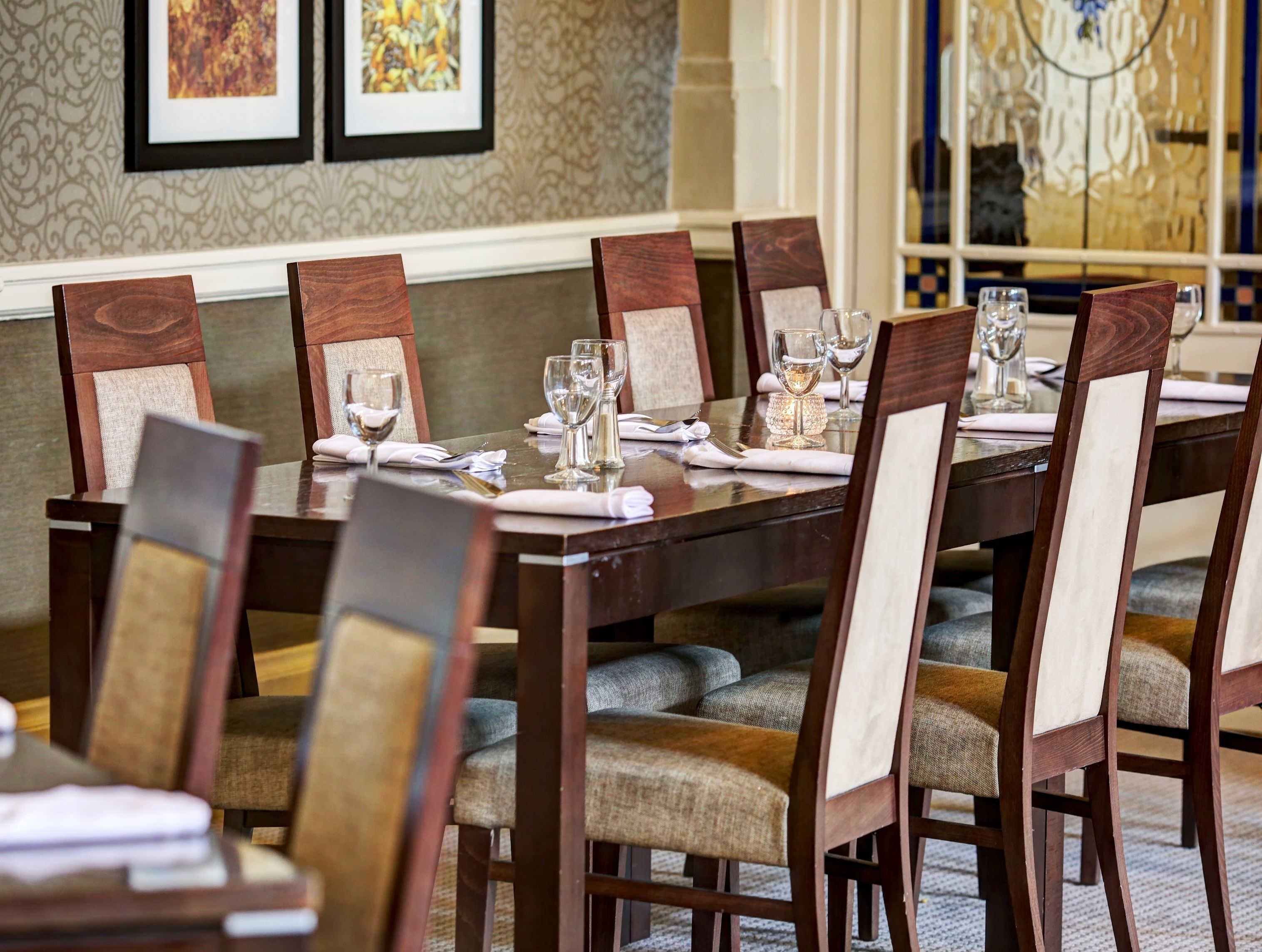Comedor con una larga mesa de madera dispuesta para seis comensales, rodeada de sillas tapizadas con listones verticales.