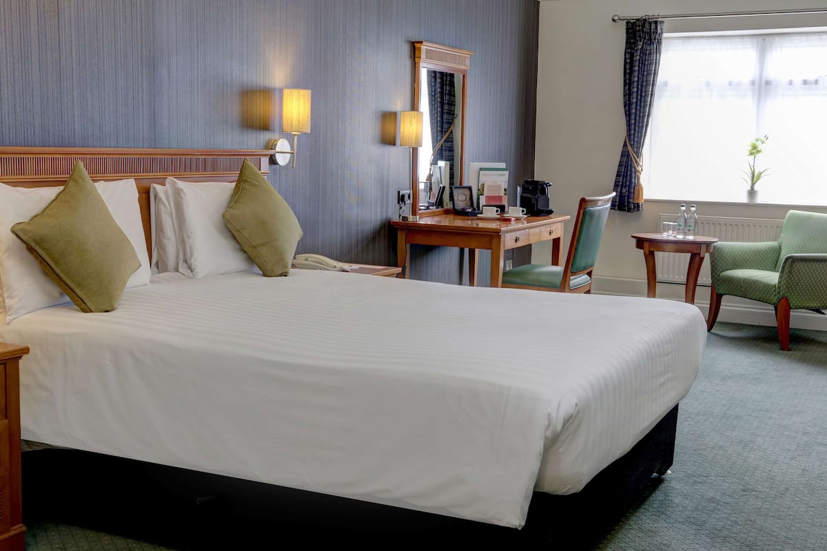 A hotel room with a large bed, a desk, a chair, a lamp, and a window with curtains.