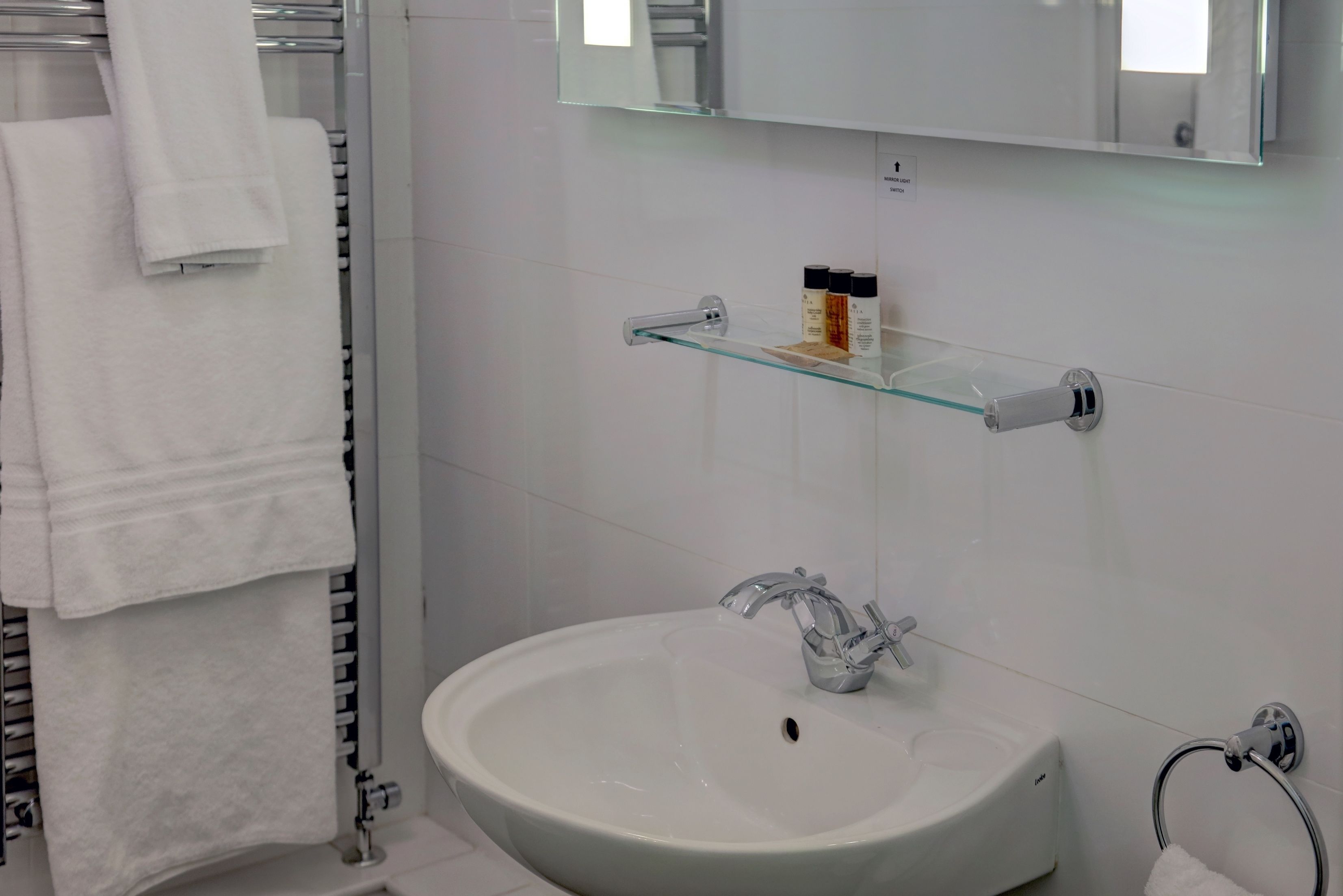 A bathroom with a white sink, a glass shelf with toiletries, and a towel rack.